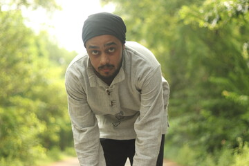 An Indian Boy wearing Khadi Kurta and a Bandana or neck gaiter standing on the road with green...
