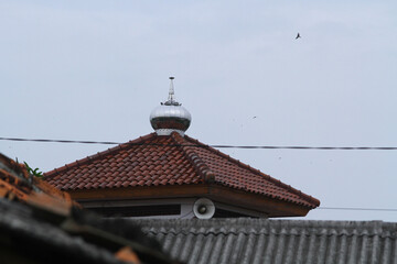 A roof tile for a mosque in West Java, Indonesia, with a blue sky and flying birds in the background