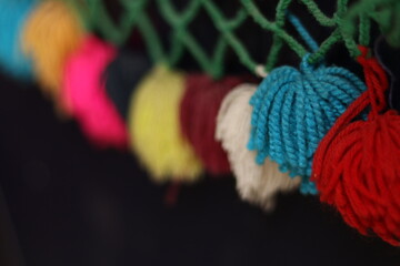 Rainbow colour Yarn Tassel Garland stitched to a piece of cloth in dark shadow
