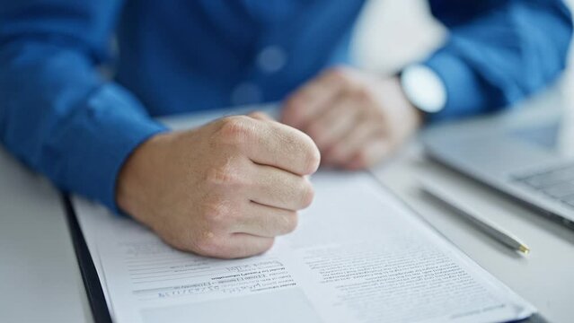 Young hispanic man business worker hitting contract with fist at the office