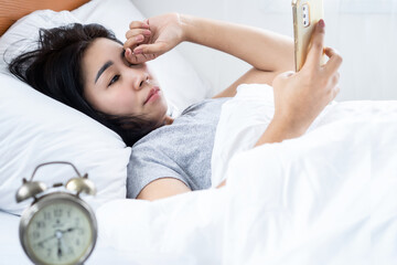 Asian woman rubbing her itchy and tired eye watching too much on mobile phone screen late at night in bed