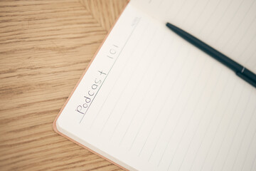 Closeup, podcast and book for write with pen for idea with mockup for mobile app, online or streaming. Writing, plan or preparation of broadcast on table for interview, question or topic for guest