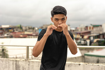 A young asian man makes a guard stance while practicing his boxing skills on the rooftop of a...