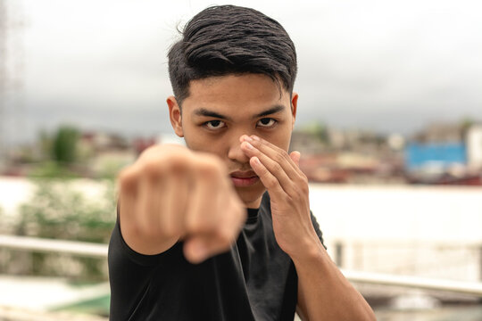 A young asian man makes a straight right hand while practicing his boxing skills on the rooftop of a building. Looking serious while doing shadowboxing training, gritty urban scene.