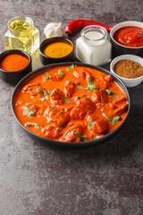 Chicken tikka masala traditional dish of indian cuisine in a black bowl with ingredients over dark concrete background closeup. Vertical