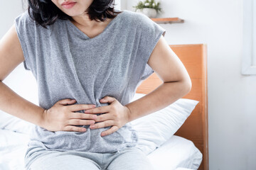 Asian woman suffering from chronic stomachache hand holding abdominal pain sitting in bed