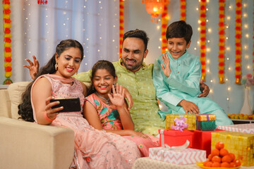 Happy young parents with sibling kids making video call on mobile phone during diwali festival for wishes at home - concept of holiday celebration, family bonding and Modern lifestyle.