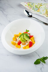 fruit salad with kiwi, strawberries, mango and nuts in a deep plate side view