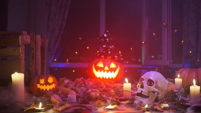 Scary Jack-o'-lantern in smoke with witch hat on head with bright glowing eyes rotate in thick fog neon red blue light, on threshold decoration Halloween holiday, during day of dead, 31 October.