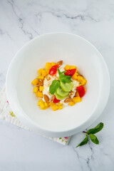 fruit salad with kiwi, strawberries, mango and nuts in a deep plate top view