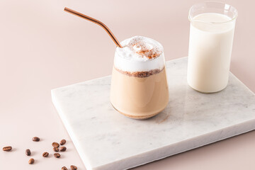 A large glass with a chocolate drink and chocolate wedges, a latte with foam on a marble white podium with a jug of milk. The perfect dessert.