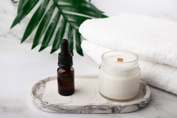 Obraz na płótnie Canvas aromatic candle with oil serum in the bathroom on a marble tray with towels, moisturizing facial skin, natural cosmetics