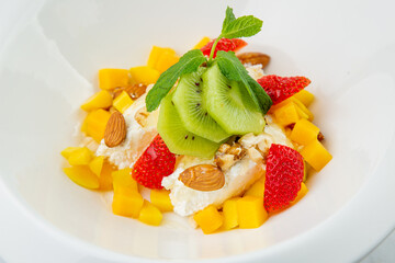 fruit salad with kiwi, strawberries, mango and nuts in a deep plate side view