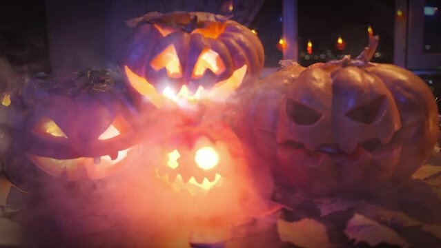 Four pumpkins glow with colorful lights, foggy festive Halloween invitation background, creepy Jack-o'-lanterns in smoke, close up.