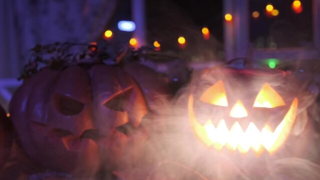 Pumpkins lanterns glowing with light from within tracking shot, scary Halloween festive background party invitation autumn decoration red and yellow color lights and garlands, in smoke.