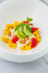 fruit salad with kiwi, strawberries, mango and nuts in a deep plate side view