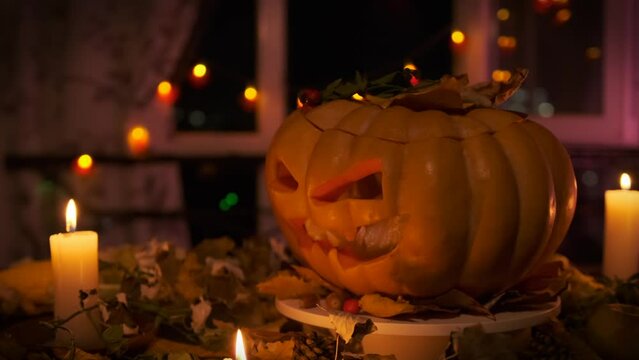 Close up slowly spin Jack-o'-lantern made carved orange pumpkin against backdrop of autumn decorations dry leaves, flickering candles, garlands, promo attracting friends to Halloween party.