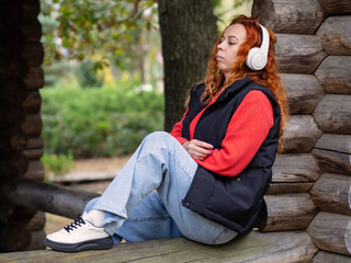 Fototapeta na wymiar A girl with headphones in the park listens to music. A young girl rests in the park on a sunny day.