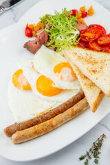 scrambled eggs with vegetables, cherry tomatoes, bread, herbs and sausages on a white plate side view