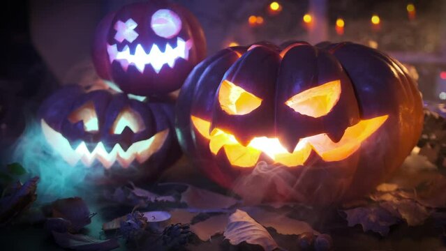 Jack-o'-lanterns are set on fire in the grounds of the house, traditional pumpkins flashing neon lights on dry leaves. Festive Halloween background invitation.
