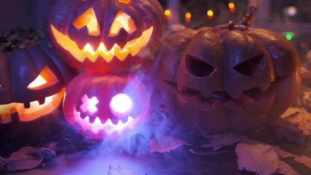 Halloween decorations with beautiful assorted carved pumpkins with creepy Jack-o-lantern smiles glowing with neon lights through the thick fog close-up tracking shot.