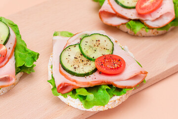Light Breakfast. Quick and Healthy Sandwiches. Rice Cakes with Ham, Tomato, Fresh Cucumber and Green Salad on Wooden Cutting Board. Beige Background