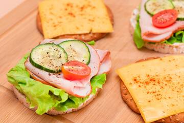Light Breakfast. Quick and Healthy Sandwiches. Rice Cakes with Ham, Tomato, Fresh Cucumber, Green Salad and Cheese on Wooden Cutting Board. Beige Background