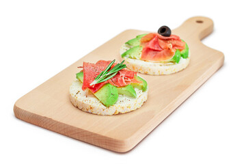 Rice Cake Sandwich with Avocado, Jamon, Olives and Rosemary on Wooden Cutting Board - Isolated on White. Easy Breakfast. Quick and Healthy Sandwiches. Crispbread with Tasty Filling - Isolation