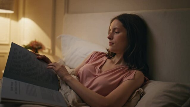 Smiling girl reading book in bed evening closeup. Relaxed woman resting bedtime