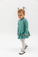 The offended girl with two ponytails in a turquoise dress with pouting lips. Kids emotion. Education concept.