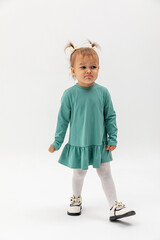 The offended girl with two ponytails in a turquoise dress with pouting lips. Kids emotion. Education concept.