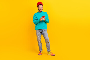 Fototapeta na wymiar Full length photo of satisfied man dressed turquoise pullover look at smartphone read notification isolated on yellow color background