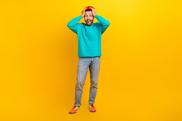 Fototapeta premium Full length photo of speechless crazy man dressed turquoise pullover holding arms on head screaming isolated on yellow color background