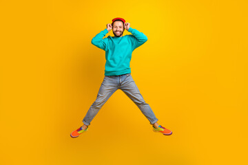Fototapeta na wymiar Full length photo of good mood positive man wear turquoise pullover flying hands touching beanie hat isolated on yellow color background