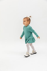 Happy little girl with two ponytails and in a turquoise dress running on white background, happiness concept