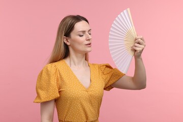 Beautiful woman waving yellow hand fan to cool herself on pink background - obrazy, fototapety, plakaty