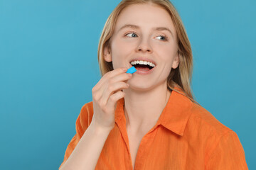Happy young woman putting bubble gum into mouth on light blue background