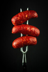 Fried Bavarian meat sausages on a fork. Tasty snack concept for hotel or restaurant on black background