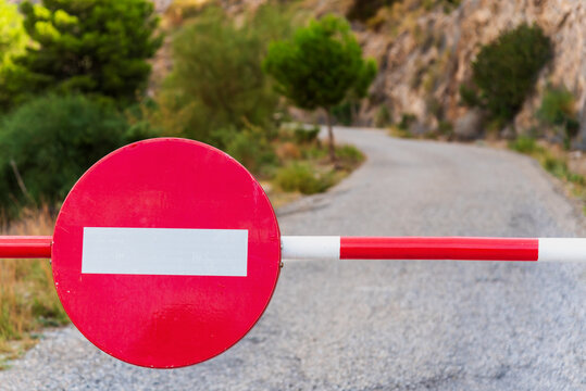 Barrier with a no entry sign with a paved country road that disappears in the background. Close-up.