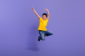 Full size photo of cute young schoolboy jumping have fun dancing dressed yellow clothes isolated on violet color background