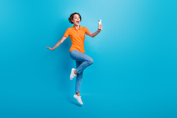 Fototapeta na wymiar Full size photo of impressed excited girl dressed stylish polo denim trousers flying look at smartphone isolated on blue color background