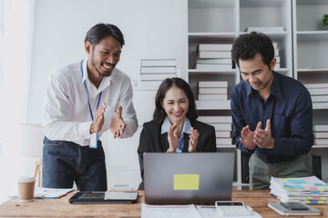 Young Asian business people raising his hand to congratulate excited and happy at a successful work with laptop computer at office