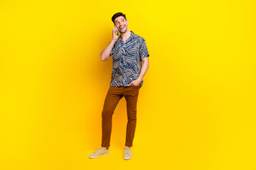 Fototapeta premium Full size photo of friendly guy wear stylish shirt trousers talk on smartphone look empty space isolated on yellow color background