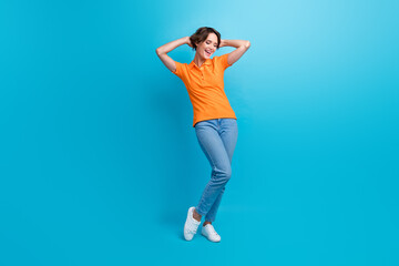 Full length photo of lovely pleasant woman wear orange t-shirt denim trousers hold arms behind head isolated on blue color background