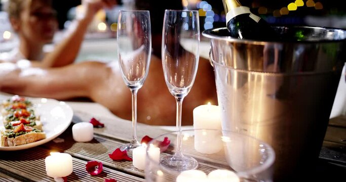 Champagne glass, food and hot tub couple talking, conversation and romantic partner bond on Valentines day date. Night, chat and marriage people relax in jacuzzi with alcohol, snack and candle flames