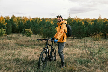  active lifestyle.A man in a protective helmet with a backpack stands with a mountain bike in the autumn forest and smiles.Mountain Bike
