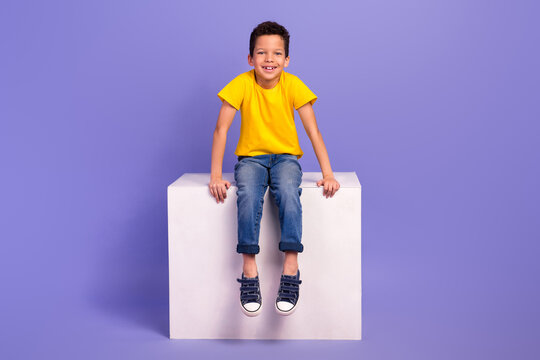 Full body photo of charming young boy sit white cube shopping promo dressed yellow outfit isolated on violet color background