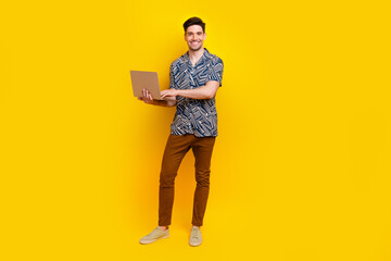 Full size photo of intelligent pleasant guy wear stylish shirt brown trousers typing email on laptop isolated on yellow color background