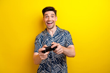 Portrait of astonished cheerful person good mood hands hold controller playing video games isolated on yellow color background - obrazy, fototapety, plakaty