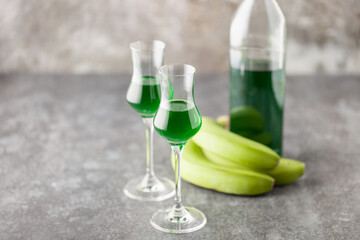 Green banana liqueur in grappas glasses and fresh  bananas on the table. Copy space